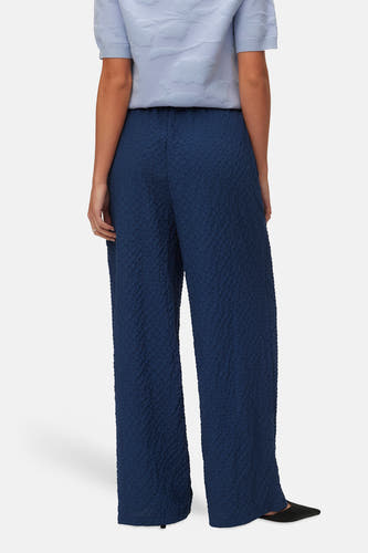 Blauwe broek van VERO MODA® met een getextureerde stof en wijde pijpen, gezien van achteren.
