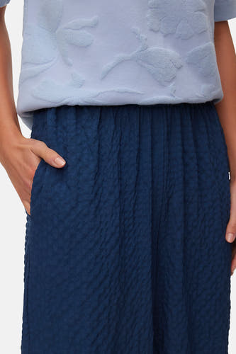 Blauwe broek van VERO MODA met geplooide tailleband en een gekreukelde textuur, met hand in de zak.