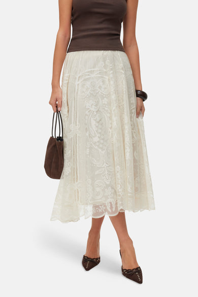 Beige lange rok van VERO MODA® met gedetailleerd kanten bloemenpatroon, gecombineerd met een bruine top en muiltjes.