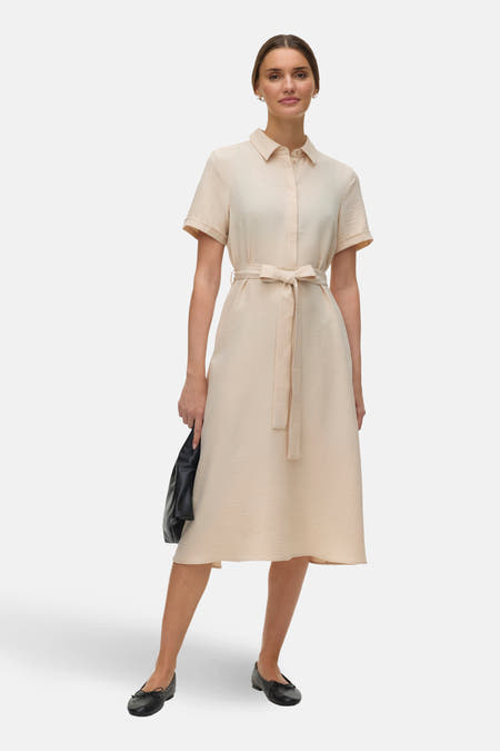 Ecru jurk met korte mouwen van Vero Moda, met een strikceintuur en zwarte platte schoenen.