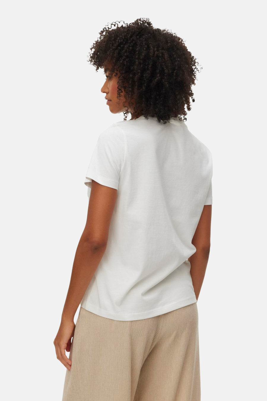 T-shirt blanc de VERO MODA, vue de dos porté par un mannequin aux cheveux bouclés foncés et un pantalon beige.