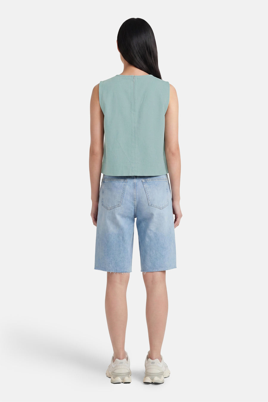 Groene mouwloze blouse van VERO MODA®, achterzijde met rits, gestructureerd materiaal, gekenmerkt door minimalistische stijl, gedragen met lichtblauwe denim shorts en witte sneakers.