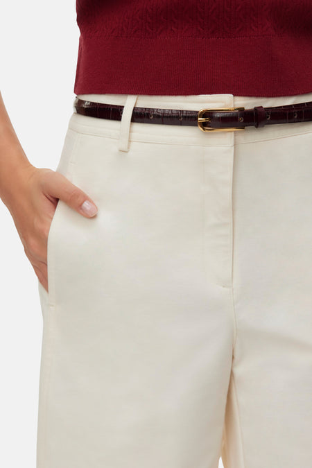 Ecru Bermuda van VERO MODA, bij de taille gedragen met een dunne donkerbruine riem met krokodillenprint en een hand in de zak.