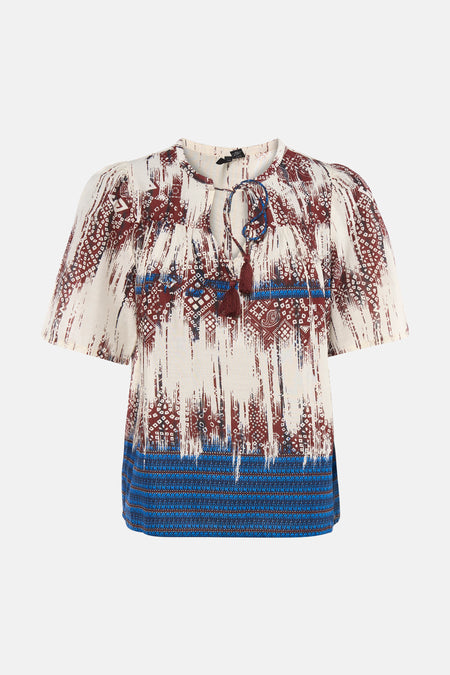Chemisier multicolore à manches courtes de VERO MODA® avec des motifs abstraits et tribaux rouges et bleus, et des pompons au col.