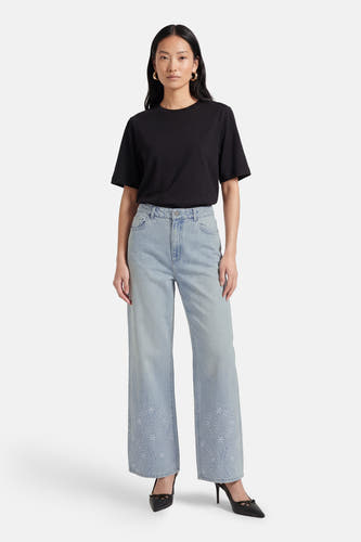 Lichtblauwe wijde jeans van Vero Moda, met geborduurde bloemen aan de onderkant, gecombineerd met een zwart T-shirt en zwarte pumps.

