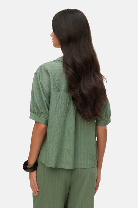 Groene blouse met korte mouwen van VERO MODA, met fijne strepen en gekreukte textuur, gedragen door een vrouw op de rug met bijpassende broek en armband.
