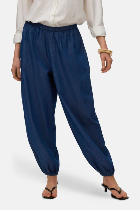 Pantalon bleu de VERO MODA, avec taille élastique et ourlet froncé, combiné avec une blouse blanche et des talons.