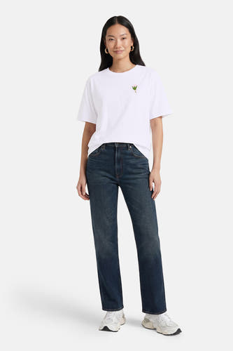 Witte korte mouwen T-shirt met klein roze bloemmotief op borst, van VERO MODA®, gedragen met donkerblauwe jeans en witte sneakers, front view.