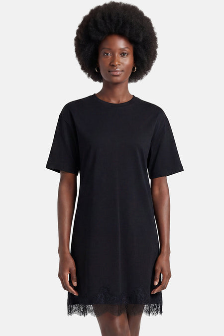 Robe noire à manches courtes de VERO MODA avec ourlet en dentelle et col rond, portée par un mannequin avec afro et boucles d'oreilles dorées.