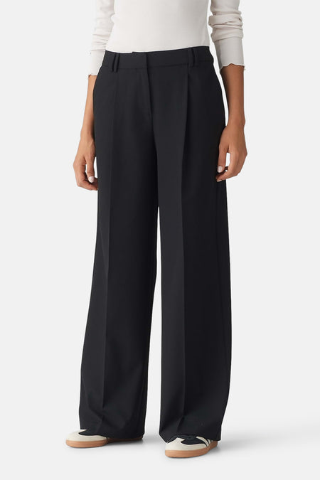 Zwarte broek van OPUS met wijde pijpen en plooien, gedragen met witte longsleeve en sneakers.