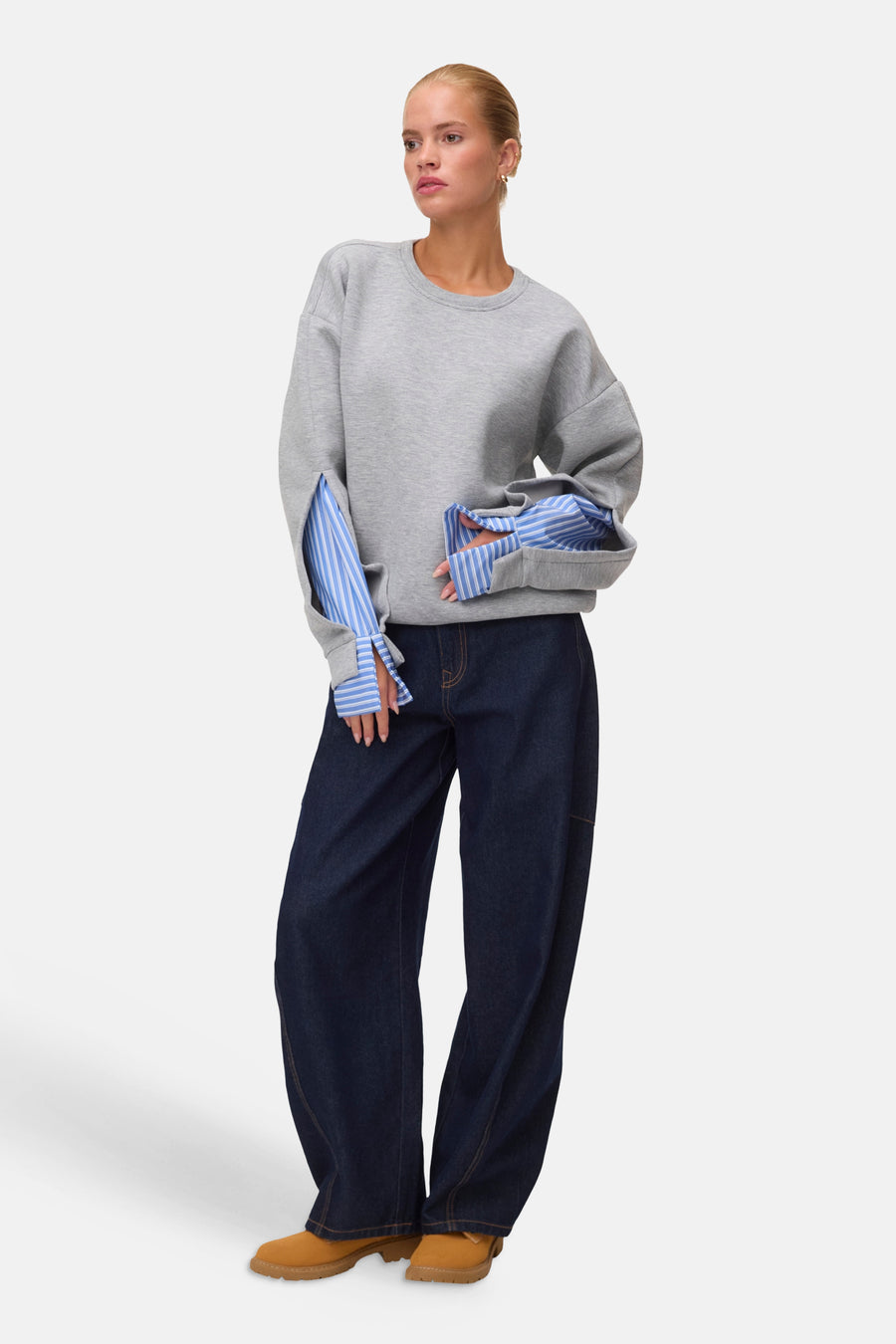 Grijze ronde hals sweater met blauw-witte gestreepte mouwen van VERO MODA®, gedragen met donkerblauwe wijde jeans en bruine laarzen, lifestyle view