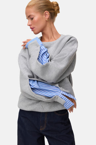 Grijze ronde hals sweater van VERO MODA® met multicolor gestreepte mouwen, gedragen over een blauw-wit gestreept shirt, zijprofiel.