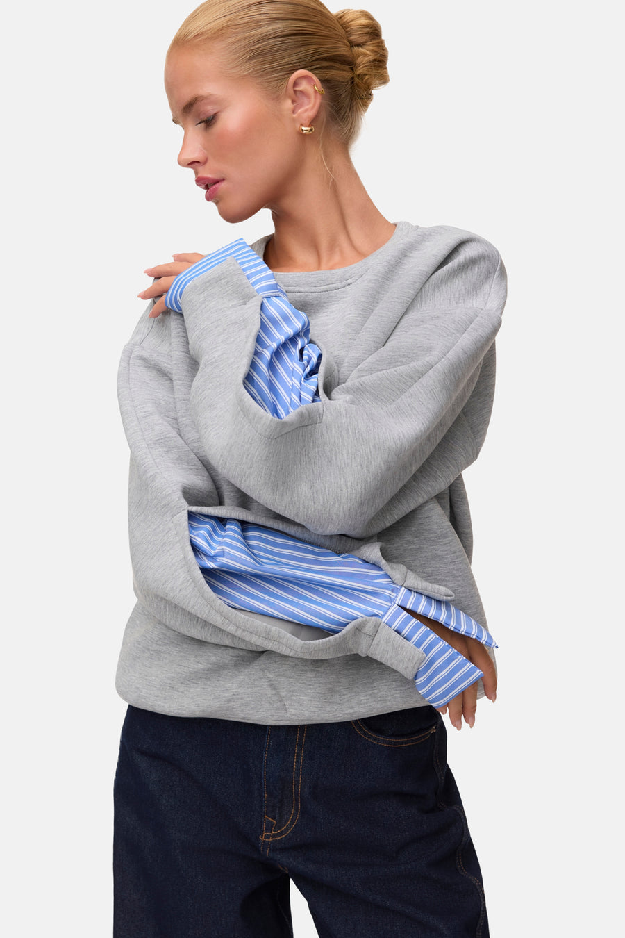 Grijze ronde hals sweater van VERO MODA® met multicolor gestreepte mouwen, gedragen over een blauw-wit gestreept shirt, zijprofiel.