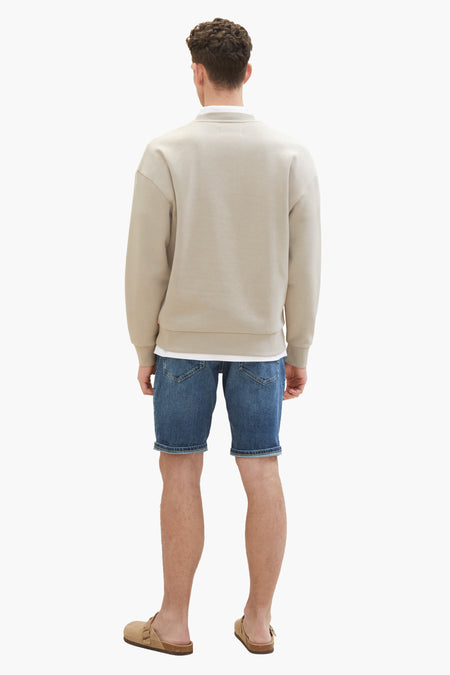 Donkerblauwe jeansshort van TOM TAILOR, gezien van achteren, gecombineerd met een beige sweater en bruine sandalen.
