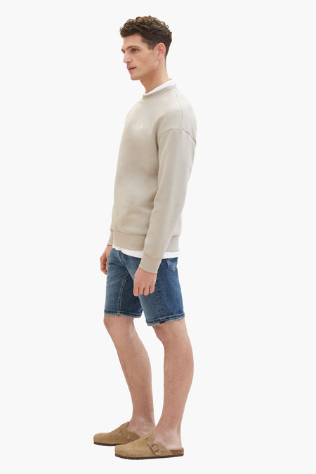 Donkerblauwe jeansshort van TOM TAILOR, gecombineerd met een beige sweatshirt en suède muiltjes, in zij-aanzicht.