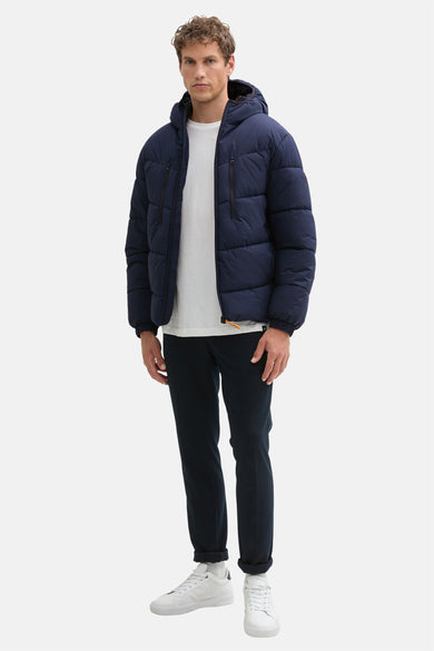 Blauwe korte jas van TOM TAILOR, met ritszakken, gedragen over een wit T-shirt en donkere pantalon met witte sneakers.
