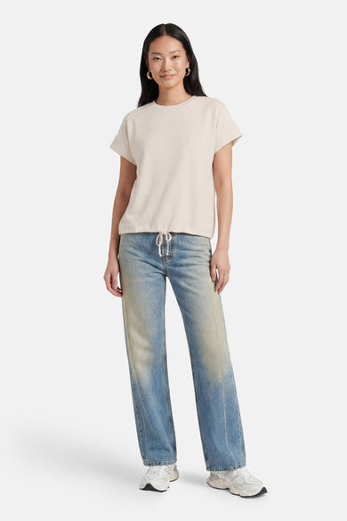 Beige korte mouwen T-shirt van OPUS met wafeltextuur, voorzien van trekkoord aan de zoom, gedragen met lichtblauwe jeans en witte sneakers.