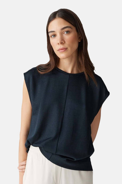 Zwarte mouwloze blouse van OPUS, met een subtiele verticale naad aan de voorkant en gedragen met een witte broek.
