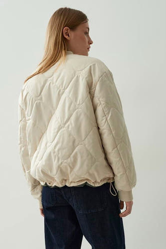 Ecru korte jas van OPUS, met een gewatteerd ruitpatroon, lange mouwen en donkere jeans.
