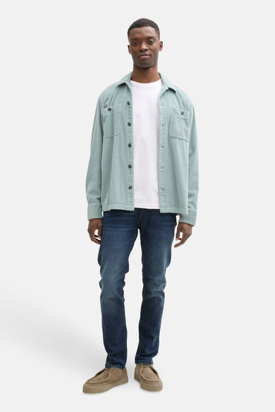 T-shirt blanc à manches courtes de TOM TAILOR, porté sous un gilet corduroy bleu clair et des jeans bleus marine avec des chaussures marron.
