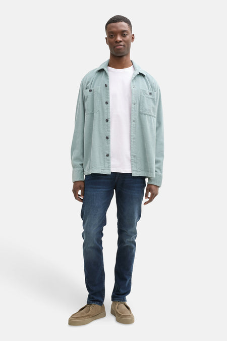 T-shirt blanc à manches courtes de TOM TAILOR, porté sous un gilet corduroy bleu clair et des jeans bleus marine avec des chaussures marron.