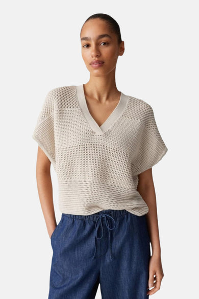 Ecrukleurige trui van OPUS, met een v-hals en een open gebreide textuur, gecombineerd met een donkerblauwe broek.
