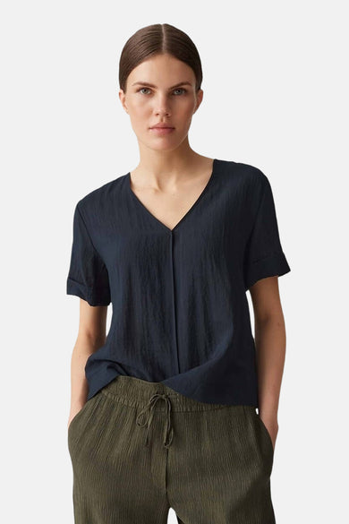 Blouse noire à manches courtes d'OPUS, avec un col V et des détails plissés, associée à un pantalon vert.