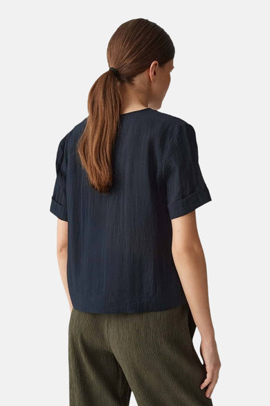 Blouse noire à manches courtes d'OPUS, dos visible, associée à un pantalon plissé.