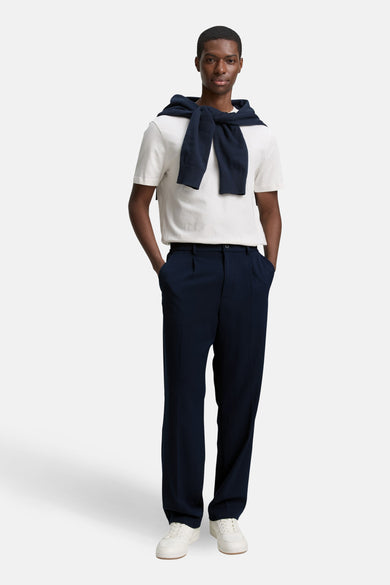 Pantalon bleu de TOM TAILOR, plissé, porté avec un t-shirt blanc et un gilet bleu marine.