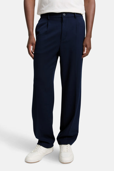 Pantalon bleu de TOM TAILOR, avec plis et une large ceche, associé à des baskets blanches.