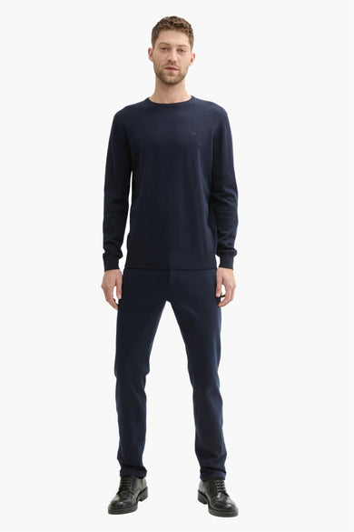Blauwe chino van TOM TAILOR, gecombineerd met een marineblauwe trui en zwarte veterschoenen.
