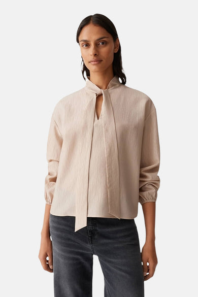 Beige blouse met lange mouwen van OPUS, met strikdetail en een subtiele textuur, gecombineerd met een grijze jeans.
