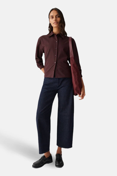 Vrouw in bruine blouse, donkere jeans en zwarte schoenen met rode tas.