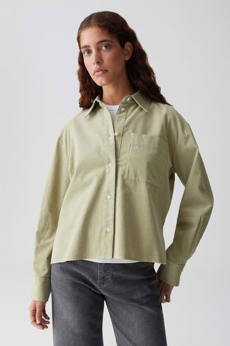 Groene blouse met lange mouwen van OPUS, met een borstzak en gedragen over een wit shirt met grijze jeans.
