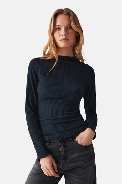 Vrouw in donkerblauwe ribgebreide top met lange mouwen en grijze jeans.