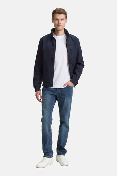 Korte blauwe jas van TOM TAILOR, gedragen met een wit T-shirt en jeans, met de hand in de zak.