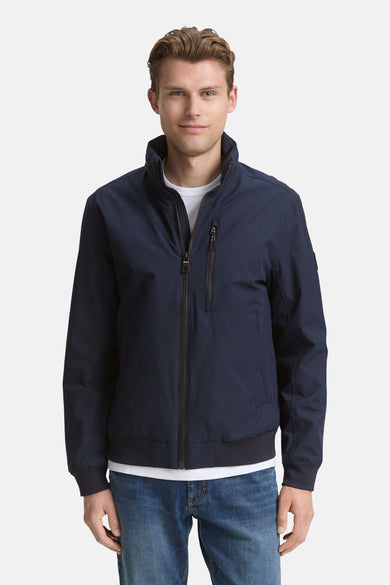 Blauwe korte jas van TOM TAILOR, met een ritssluiting en een opstaande kraag, gedragen over een wit T-shirt en blauwe jeans.