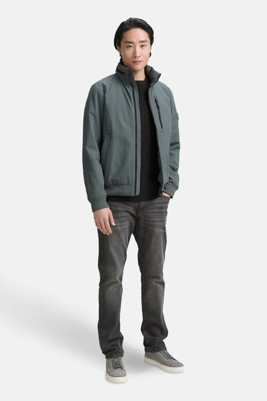 Korte groene jas van TOM TAILOR, met zwarte trui en grijze jeans en schoenen.