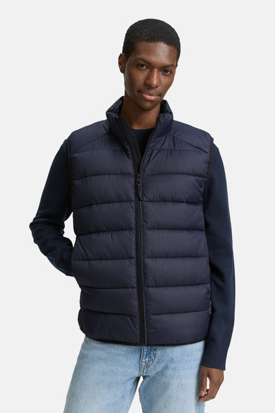 Gilet bleu de TOM TAILOR, porté sur un sweat-shirt bleu marine et une légère jean.