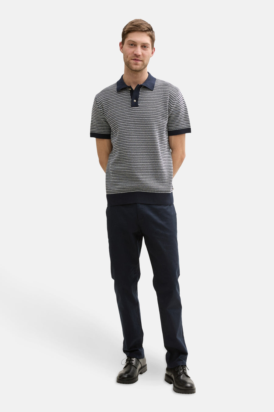 Een man in een gestreepte polo, donkerblauwe broek en zwarte schoenen.