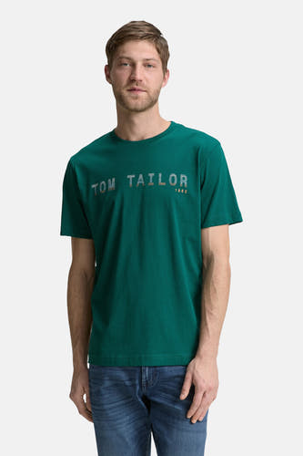 Groen T-shirt met korte mouwen van Tom Tailor, met bedrukte tekst en gedragen met een blauwe jeans.
