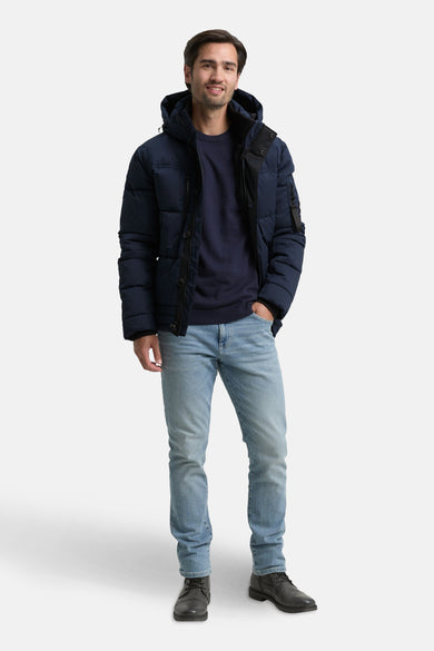 Manteau court bleu de TOM TAILOR, avec capuche, porté avec des jeans et des chaussures noires.