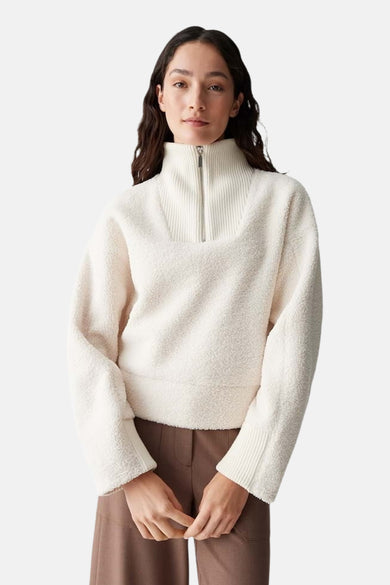 Ecru trui van OPUS, met een hoge kraag voorzien van een ritssluiting, gecombineerd met een bruine pantalon.
