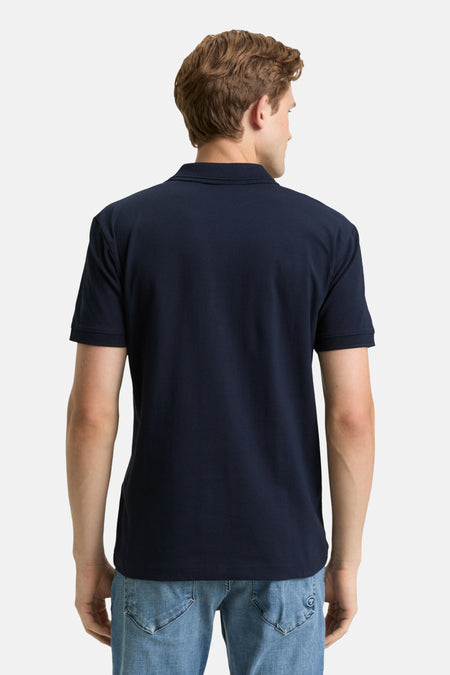 Man achterkant, marineblauw poloshirt, jeans.
