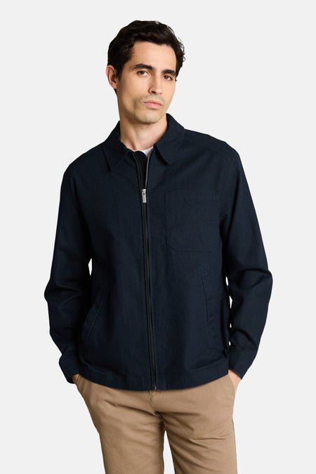 Veste bleue de TOM TAILOR, portée sur un t-shirt blanc et un short marron avec des baskets blanches.