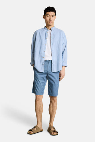 Blauwe bermuda van TOM TAILOR, gedragen met een wit T-shirt en een lichtblauw linnen overhemd, gecombineerd met bruine sandalen.