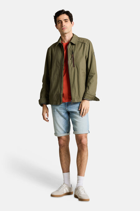 Jeansshort van lichtblauw denim van TOM TAILOR, gecombineerd met een kaki jas en witte sneakers.
