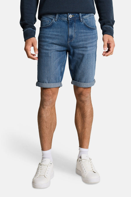 Jeansshort van denim in middenblauw van TOM TAILOR, met opgerolde pijpen, gecombineerd met witte sneakers en sokken.