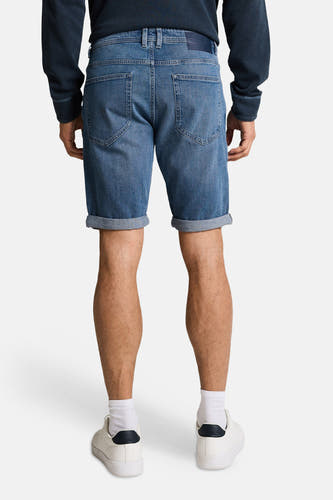 Jeansshort in middenblauw denim van TOM TAILOR, gezien van achteren, met opgerolde pijpen en witte sneakers met sokken.