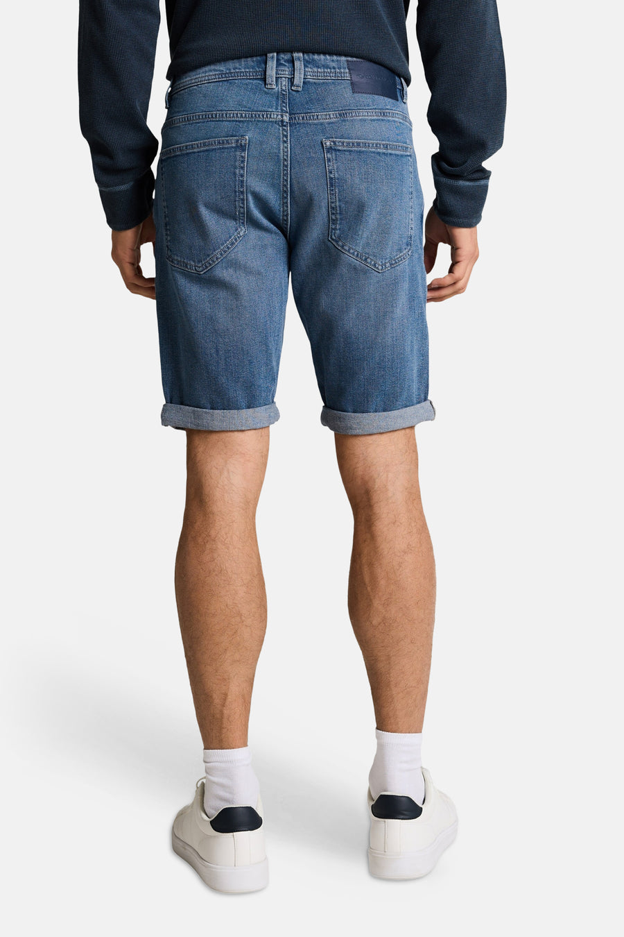Jeansshort in middenblauw denim van TOM TAILOR, gezien van achteren, met opgerolde pijpen en witte sneakers met sokken.